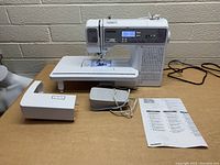 Front view of Brother SQ9285 sewing machine with wide table attachment, foot pedal, and instruction manual on a table.