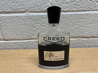 Front view of Creed Aventus cologne bottle showing the logo, black textured label, and horse and rider emblem with 'AVENTUS' text.