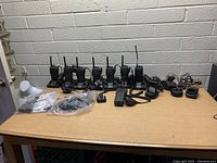 Wide shot of entire lot, showing multiple walkie talkies and various accessories laid out on table against white brick wall background.