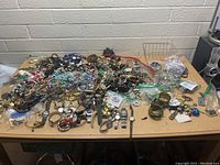 Overview of the large lot showing a spread of assorted jewelry items and beads on a table in front of a white brick wall.