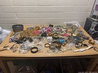 Wide view of table filled with jewelry including bracelets, watches, beads, and small accessories in various colors and materials.