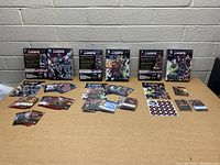 Photo of all three DC Deck-Building Game Crisis expansion packs laid out with multiple card piles and rulebooks visible.