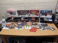 Four DC Comics deck building games with boxes open showing cards and tokens, cards laid out on table.
