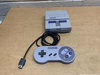 Full view of the console and the wired controller with action buttons and D-pad. Both items placed on a wooden surface showing size and condition.
