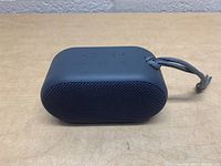 Front side view showing black mesh speaker grille and compact oval shape.
