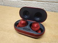 Red Samsung wireless earbuds inside open charging case showing earbuds and charging pins, with L and R buttons visible.