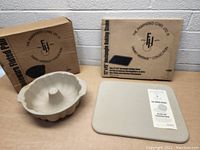 Fluted baking pan, rectangular baking stone and their boxes on table.