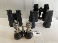 Front angle view of all three binoculars, showing the full bodies and leather strap on ERRES model