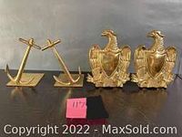 Two pairs of brass bookends side by side: one pair shaped like crossed anchors on rectangular bases, another featuring eagles with shields.