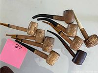 Photo of nine assorted smoking pipes on a white surface, showing corn cob texture and wooden chambers with attached shafts and mouthpieces.