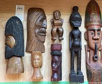 Photo showing seven wooden indigenous statues arranged side by side, viewed from the front with clear detail of carved and painted features.