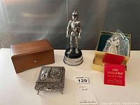 Photo showing all four items: Thorens wooden music box, metal knight figurine, silverplate/pewter music box, and boxed 1992 Kirk Stieff musical Christmas bell.