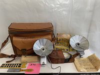 Photo showing entire lot with two flash attachments, flashbulb boxes, light meter, magnifying glass, brushes, camera bag, and instruction envelope.