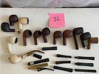 Overview of 11 pipe bowls and 15 stems/mouthpieces on white surface