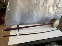Full view of Surud bowed string instrument and bow on white surface, showing length and shape
