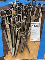 Overview of eleven tailor scissors of various sizes and brands, laid on a table with some showing rust and age wear.