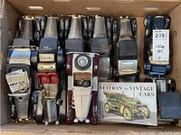 Box of vintage-style metal and plastic car models with a vintage car book included, visible whole lot from top down.