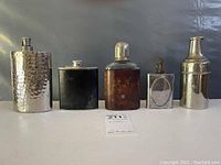 Front view of five vintage flasks and containers showing varying shapes, materials and aged condition.