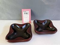 Front view of two royal maroon porcelain ashtrays with black interior on grey background