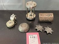 Photo showing all items including hand click counters, badges, lock, and hourglass paperweight arranged on dark surface.