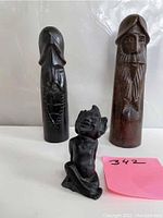 Front view of two dark wood Viking fighter carvings and small black composite elf figurine with pink note.