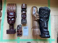 Top view of all seven wooden carved statues of indigenous peoples on wooden floor showing size and detail