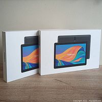 Two MAGCH 10-inch Android tablets in factory packaging, boxes resting upright on a wooden surface.