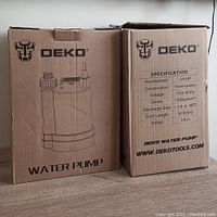 Two DEKO water pump boxes showing packaging and specifications including horsepower, construction, voltage, max flow, discharge size, and cord length.