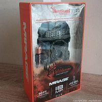 Front view of Wildgame Innovations Mirage IR 18MP trail camera sealed in original packaging, visible through clear plastic with included battery.