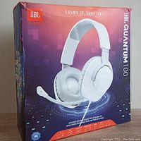 Box of JBL Quantum 100 wired over-ear gaming headset showing image of headphones and removable mic, branding and model information.