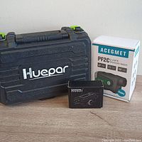 Lot overview with Huepar branded hard case, Acegmet PF2C rangefinder box, and Feyachi compact laser sight box on wooden surface