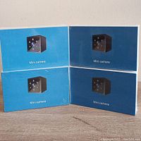 Four sealed boxes of mini cameras stacked on a wooden surface showing front with camera image.