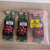Three Hardtec AMD Radeon graphics cards displayed on a wooden surface, two cards out of bag and one inside pink anti-static bubble bag with ESD caution label.