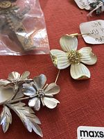Close-up photo of silver-tone floral pin and white enamel and gold floral brooch on red background