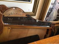 Close-up of the back and top side of the etched mirror showing floral etching and scalloped top edge, mounted on wooden dresser with some veneer missing.