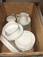 Top-down view of the set in a box showing various pieces including gravy boat with underplate, creamer, sugar bowl with lid, stack of plates and serving dish.