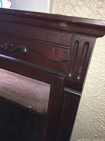 Close-up image of the upper left corner of the dresser's wooden frame showing carved decorative molding and wood grain.