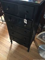 Front view of small black painted wooden chest of drawers with four drawers and wear signs.