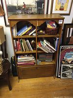 Front view of the light wood bookcase showing open shelves filled with books and a locked storage compartment at the bottom with a notice tag numbered 351.