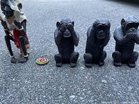 Front view of the entire set showing the three monkeys, the seated figure and the beaded ornament on concrete ground.