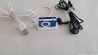 Blue Apple iPod Shuffle with white USB dock and black wired headphones from front view