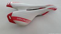 Side view of Specialized Toupe 130 bike saddle showing white and red colors, branding, and slim aerodynamic shape.
