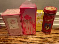 Front view of four unopened boxed perfumes on a wooden surface: Oscar de la Renta Rose, Juicy Couture Lair du Temps, Nina Ricci, and Versace Red Jeans in a tin.