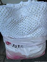 Folded white wool crocheted blanket with a lace-like crochet pattern placed on top of a pink and white plastic bag.
