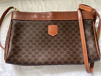 Front view of brown coated canvas body with repeating Triomphe pattern, tan leather trim and attached leather strap