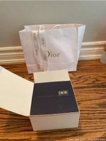Opened white Dior branded box with a black insert and Dior tag inside, for brooch packaging.