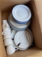 Top view of stacked white plates with blue rim, including salad plates, dinner plates, and cups.