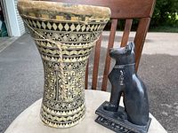 Front view of the decorative wood drum and soapstone cat sculpture on chair outdoors.