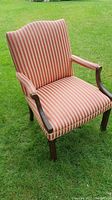 Front and left angle view of the upholstered striped accent chair outdoors on grass.