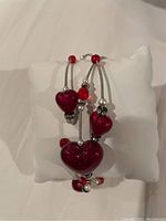 Murano glass bracelet showing three red heart-shaped beads, round red beads, and small white beads on silver-tone wires with a white display pillow.
